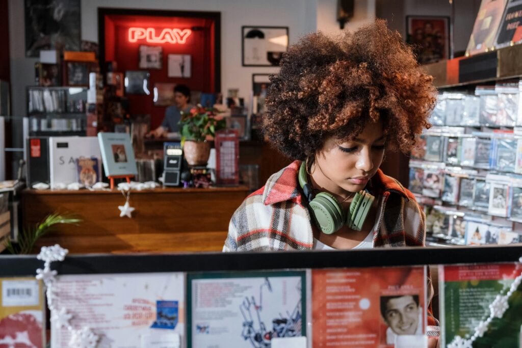 A young woman with curly hair listens to music while browsing CDs in a vibrant record store.